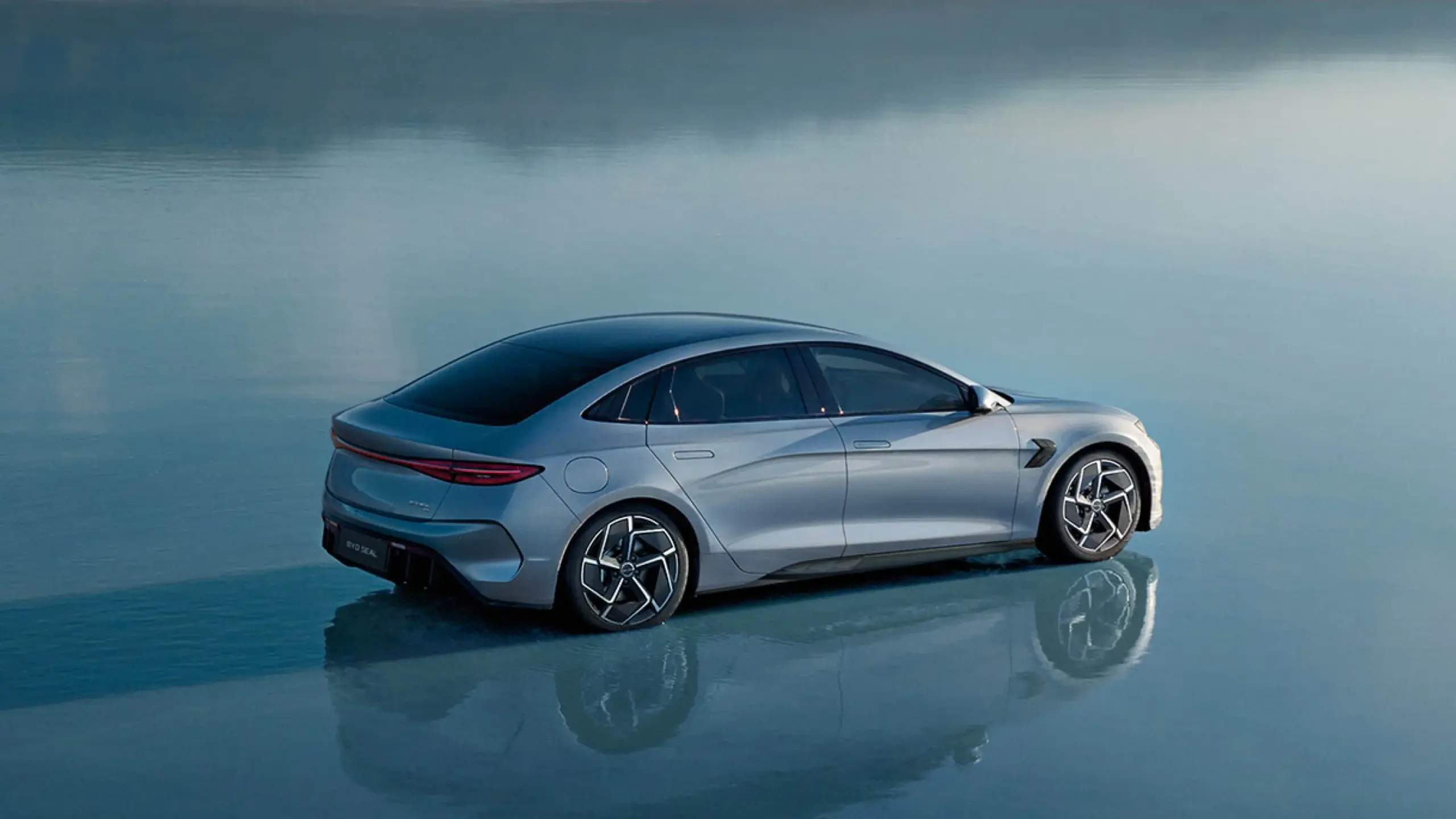 Heck- und Seitenansicht des vollelektrischen BYD Seal in blauer Lackierung, stehend auf spiegelglattem Untergrund.