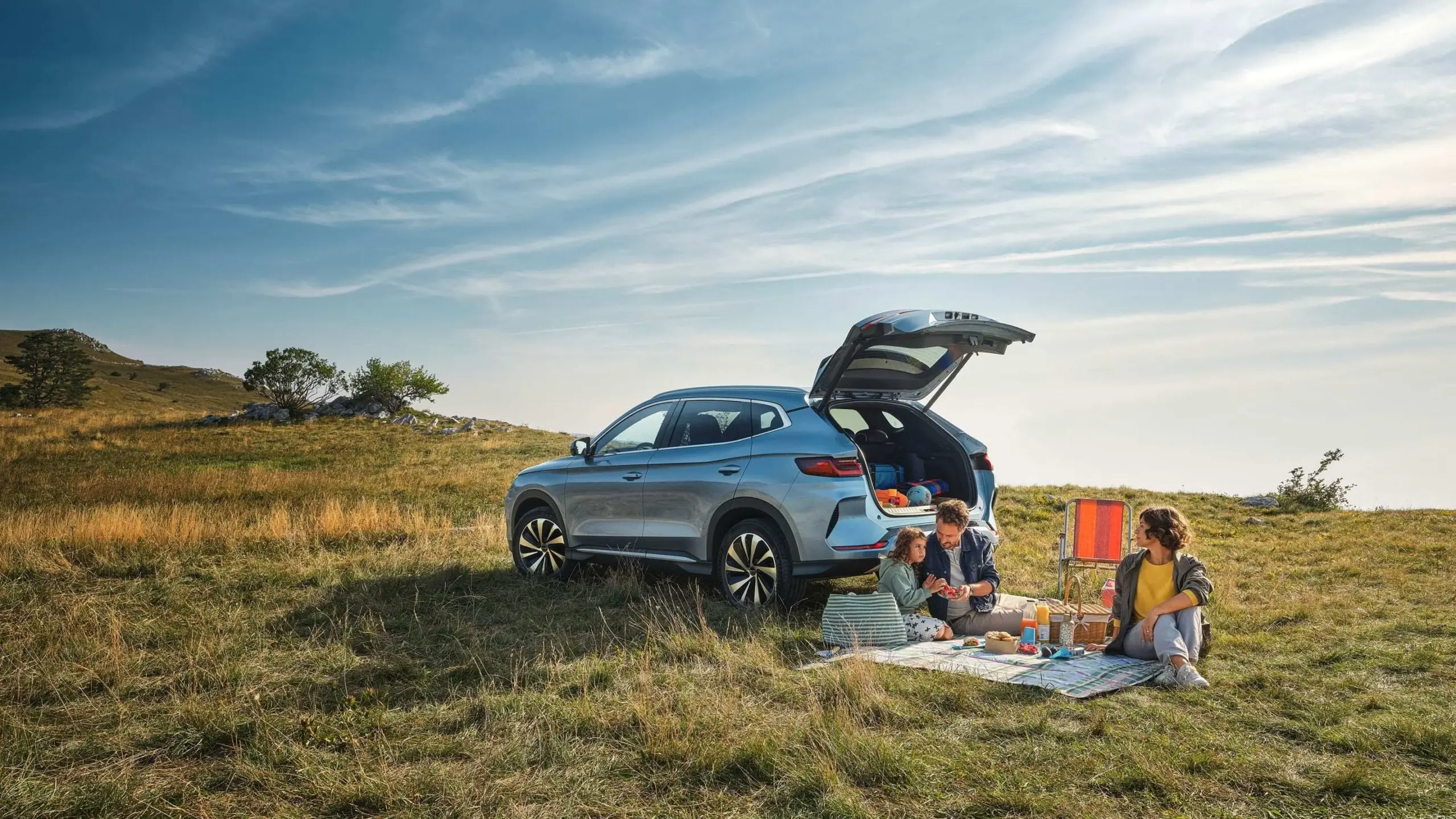 Familie beim Picknick neben einem BYD SEAL U Elektro-SUV mit offenem Kofferraum in einer Wiesenlandschaft.