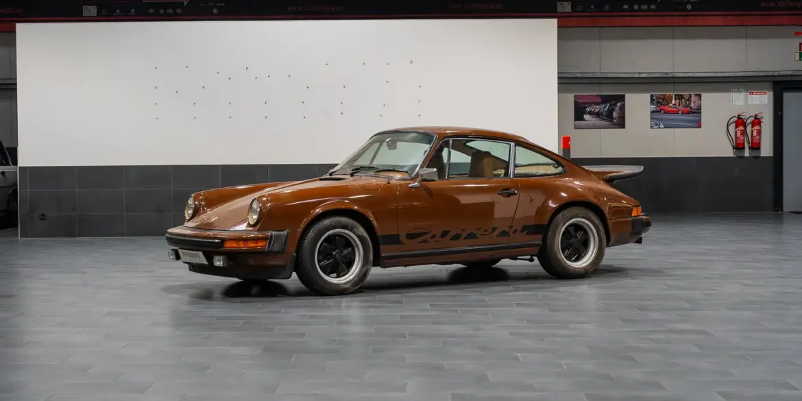 Seitenansicht eines braunen Porsche 911 G Coupé in einer Ausstellungshalle, unrestaurierter Zustand.