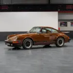 Seitenansicht eines braunen Porsche 911 G Coupé in einer Ausstellungshalle, unrestaurierter Zustand.