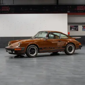 Seitenansicht eines braunen Porsche 911 G Coupé in einer Ausstellungshalle, unrestaurierter Zustand.