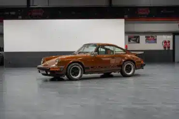 Seitenansicht eines braunen Porsche 911 G Coupé in einer Ausstellungshalle, unrestaurierter Zustand.