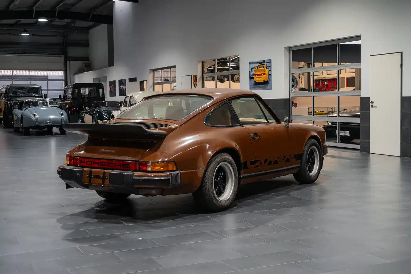 Heckansicht eines braunen Porsche 911 Carrera aus den 1970er Jahren, nicht fahrbereit, in einer Oldtimer-Garage ausgestellt.