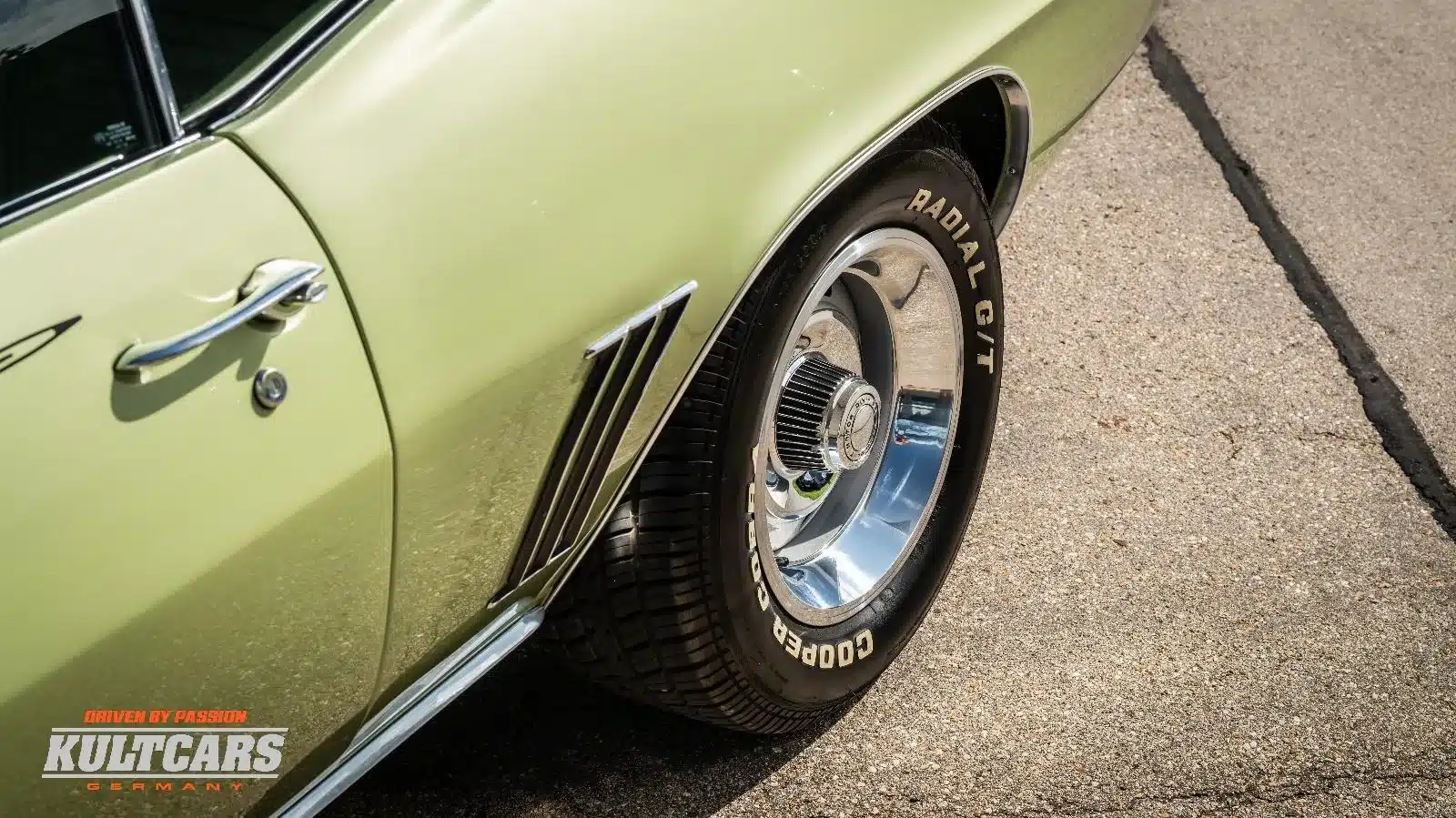 Detailaufnahme eines Chevrolet Camaro 350 V8 von 1969 in grüner Metallic-Lackierung mit verchromtem Rad und typischem Emblem.