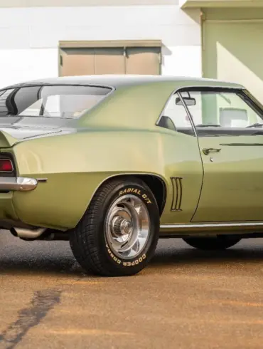 Seiten- und Heckansicht eines klassischen Chevrolet Camaro 350 V8 Coupé von 1969 mit grüner Metallic-Lackierung, geparktem Fahrzeug vor moderner Halle