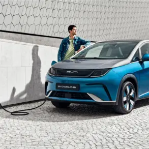 BYD Dolphin wird an einer Ladestation geladen, Mann lehnt sich an das Fahrzeug, modernes urbanes Umfeld.