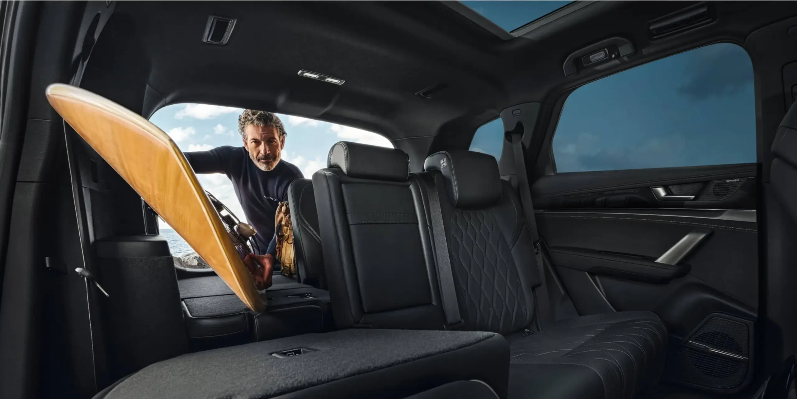 Blick in den geräumigen Innenraum des BYD Tang Elektro-SUV mit umgeklappter Sitzreihe und einem Mann, der ein Surfbrett einlädt.