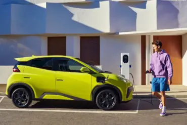 BYD Dolphin Surf Elektroauto in Gelb beim Ladevorgang an einer Wallbox vor einem modernen Gebäude.