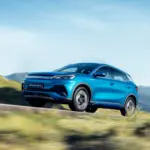 Blauer BYD Atto 3 Elektro-SUV fährt dynamisch auf einer Straße in landschaftlicher Umgebung mit Bergen im Hintergrund.