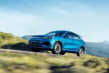 Blauer BYD Atto 3 Elektro-SUV fährt dynamisch auf einer Straße in landschaftlicher Umgebung mit Bergen im Hintergrund.