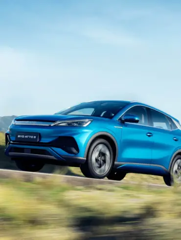 Blauer BYD Atto 3 Elektro-SUV fährt dynamisch auf einer Straße in landschaftlicher Umgebung mit Bergen im Hintergrund.