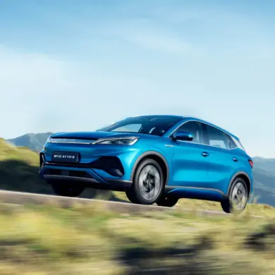 Blauer BYD Atto 3 Elektro-SUV fährt dynamisch auf einer Straße in landschaftlicher Umgebung mit Bergen im Hintergrund.