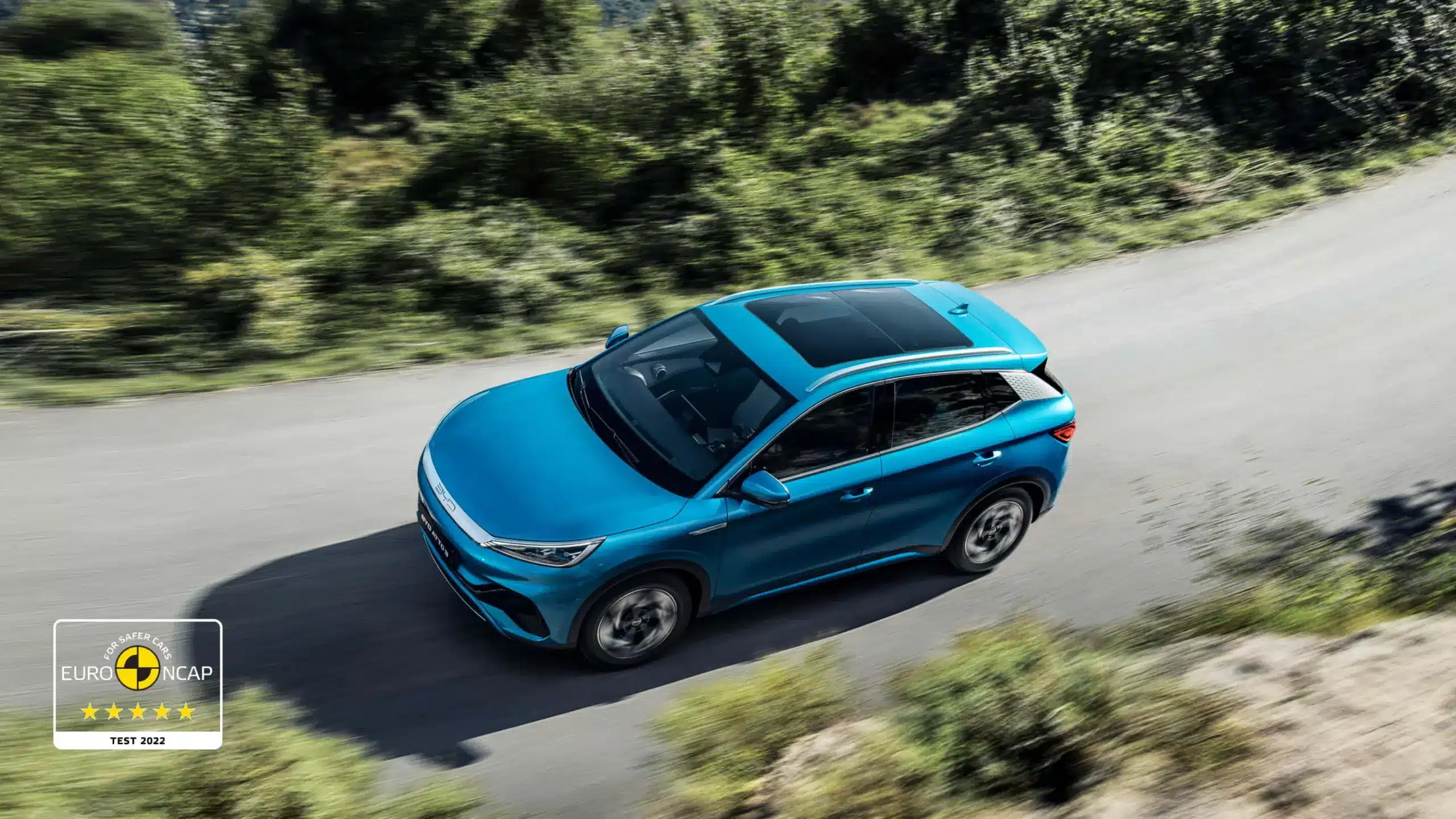 Blauer BYD Atto 3 fährt auf Landstraße, Ansicht von oben, Euro NCAP 5-Sterne-Logo sichtbar.