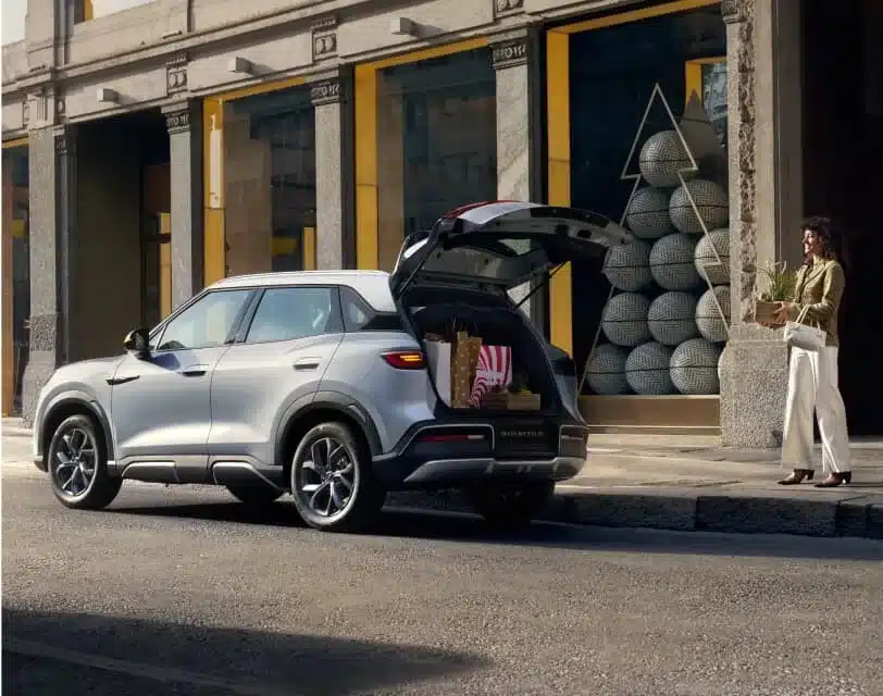 BYD ATTO 2 silberner Kompakt-SUV steht am Straßenrand mit geöffnetem Kofferraum, eine Frau trägt Einkäufe.