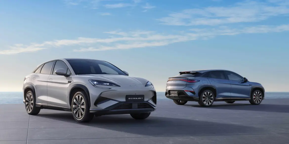 Zwei BYD SEALION 7 Elektro-SUVs stehen vor maritimer Kulisse auf einer Plattform, einer von vorn, einer von hinten.