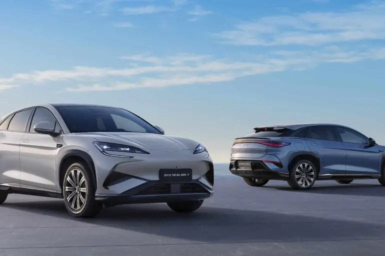Zwei BYD SEALION 7 Elektro-SUVs stehen vor maritimer Kulisse auf einer Plattform, einer von vorn, einer von hinten.