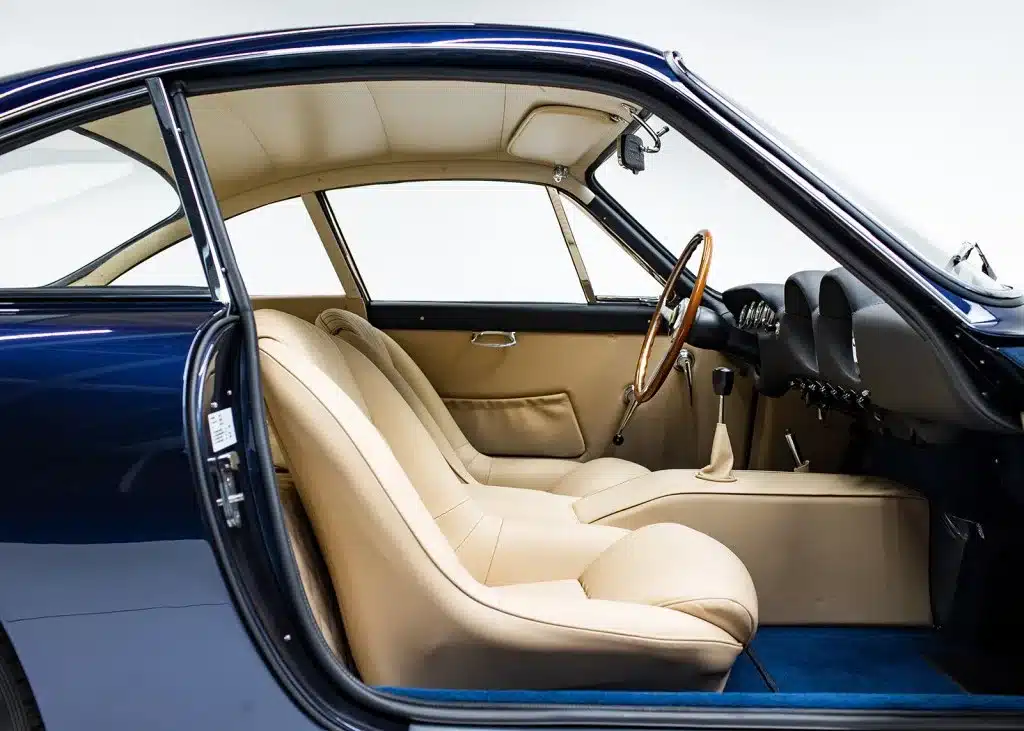 Innenansicht eines Ferrari 250 GT Lusso mit beiger Lederausstattung und Holzlenkrad, aufgenommen durch die offene Fahrertür.