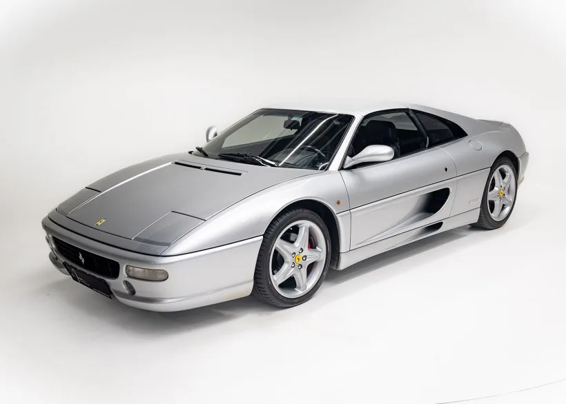 Silberner Ferrari 355 F1 GTS auf weißem Hintergrund, Front- und Seitenansicht des Sportwagens.