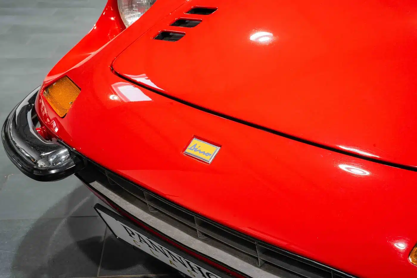 Rote Motorhaube eines Ferrari Dino 246 GT Typ M mit gelb-blauem Dino-Emblem und Scheinwerferausschnitt, Detailaufnahme