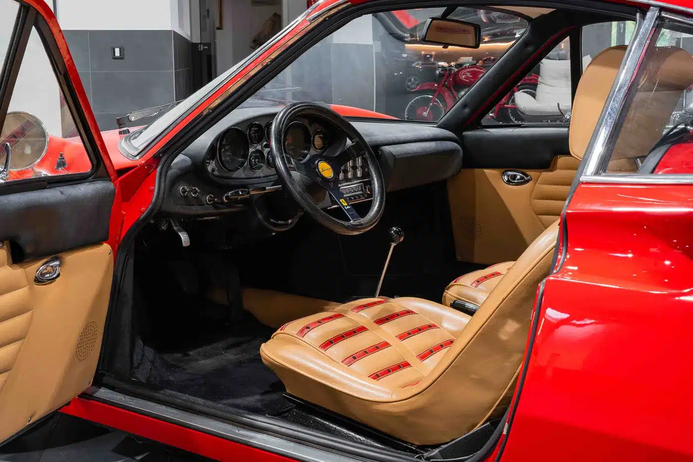 Ferrari Dino 246 GT Typ M, Baujahr 1971, mit geöffnetem Fahrerfenster, beigen Daytona-Sitzen mit roten Akzenten und schwarzem Armaturenbrett.