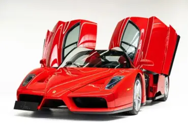 Ferrari Enzo Supersportwagen in Rot mit geöffneten Flügeltüren vor weißem Hintergrund.