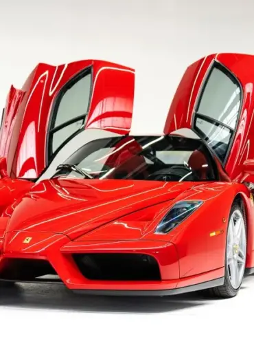 Ferrari Enzo Supersportwagen in Rot mit geöffneten Flügeltüren vor weißem Hintergrund.