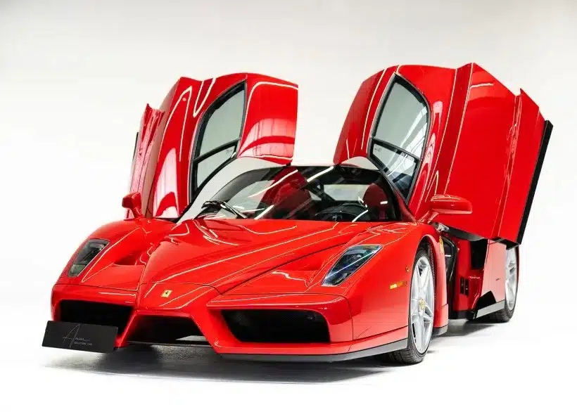 Ferrari Enzo Supersportwagen in Rot mit geöffneten Flügeltüren vor weißem Hintergrund.