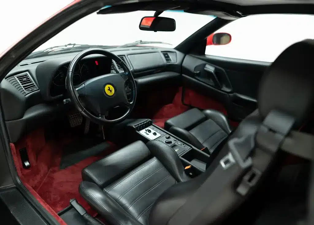 Innenansicht eines Ferrari F355 F1 GTS mit schwarzem Lederinterieur und typischem Lenkrad-Emblem.