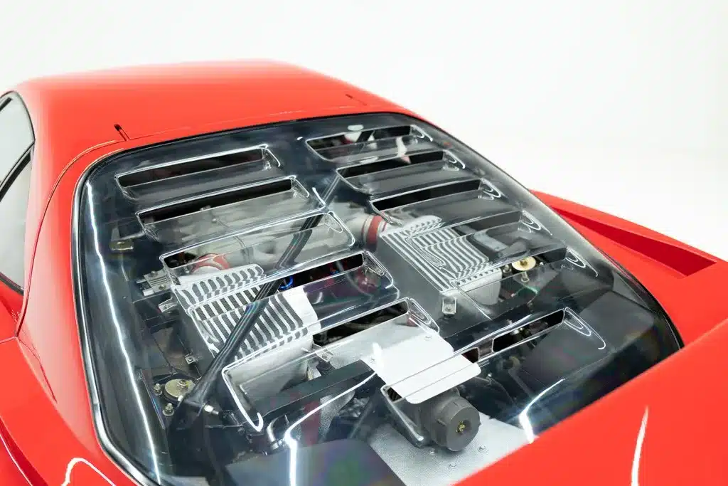Motorraum eines roten Ferrari F40 mit sichtbarem V8-Biturbo unter transparenter Haube