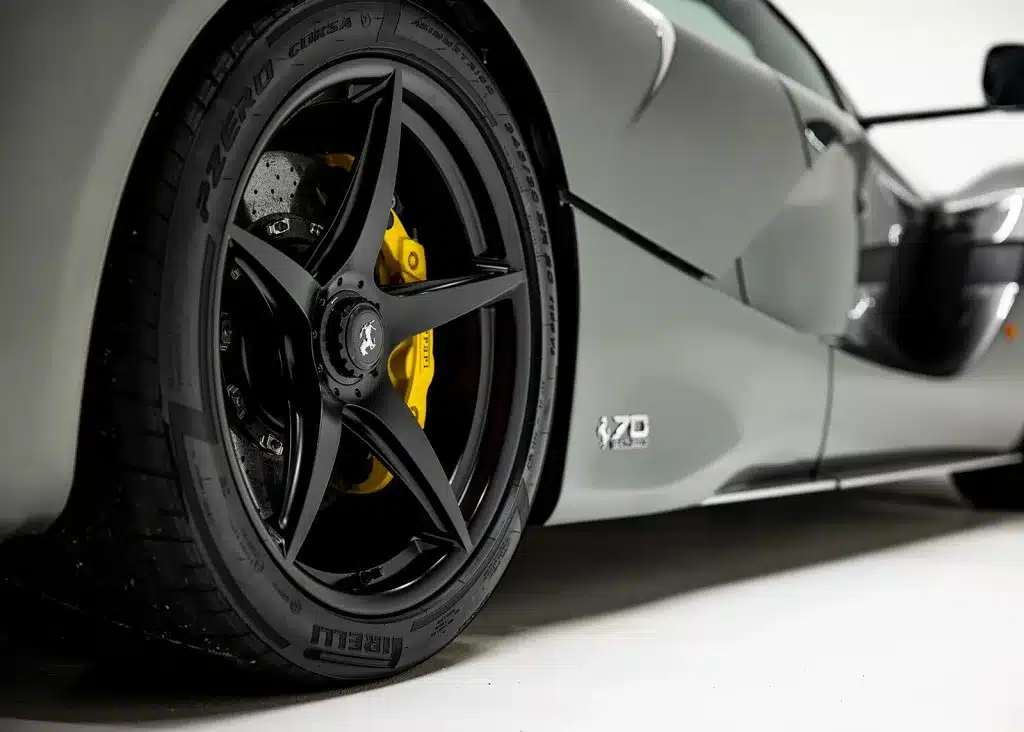 Seitliche Detailaufnahme eines schwarzen Ferrari-LaFerrari-Aperta-Rads mit gelbem Bremssattel und 70-Jahre-Emblem auf silbergrauer Karosserie