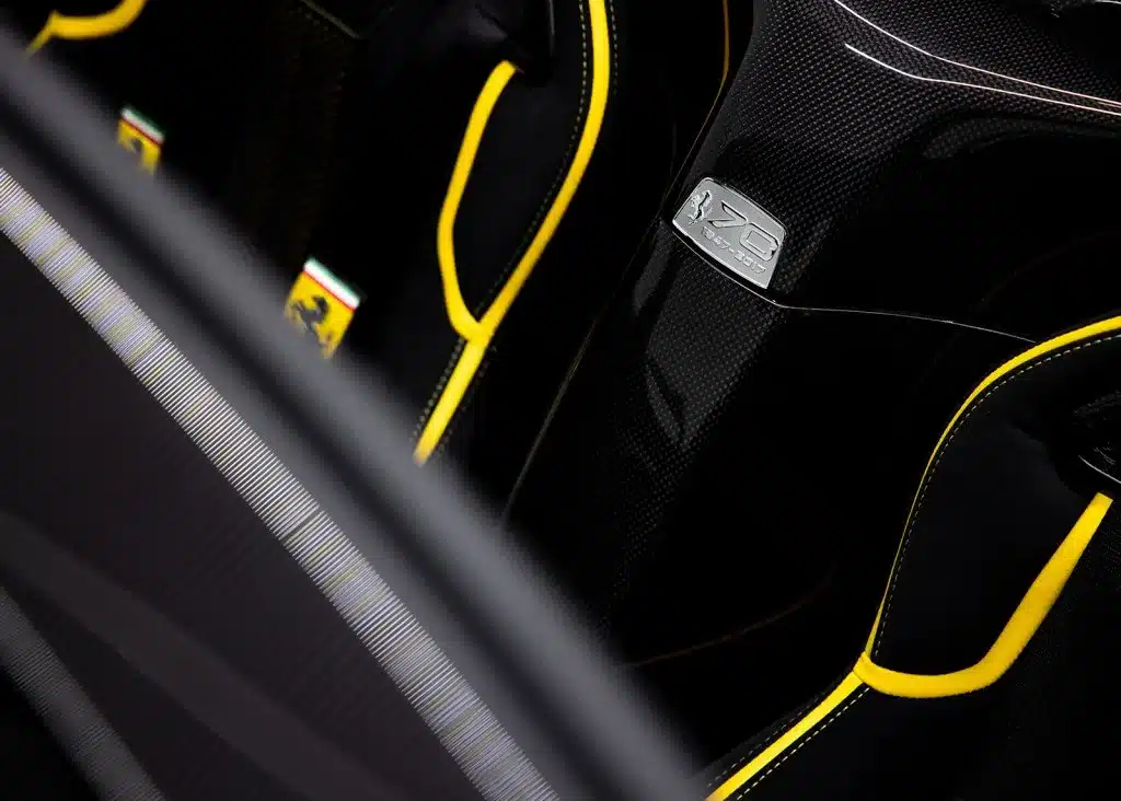 Nahaufnahme der Sportsitze und 70-Jahre-Plakette im Innenraum des Ferrari LaFerrari Aperta mit gelben Nähten.
