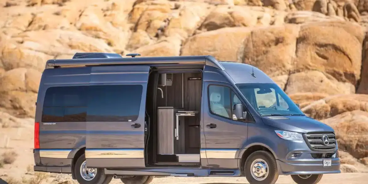 Grech Terreno-ion AWD Kastenwagen auf Mercedes-Benz Sprinter-Basis in der Wüste, seitliche Aussicht mit geöffneter Schiebetür.