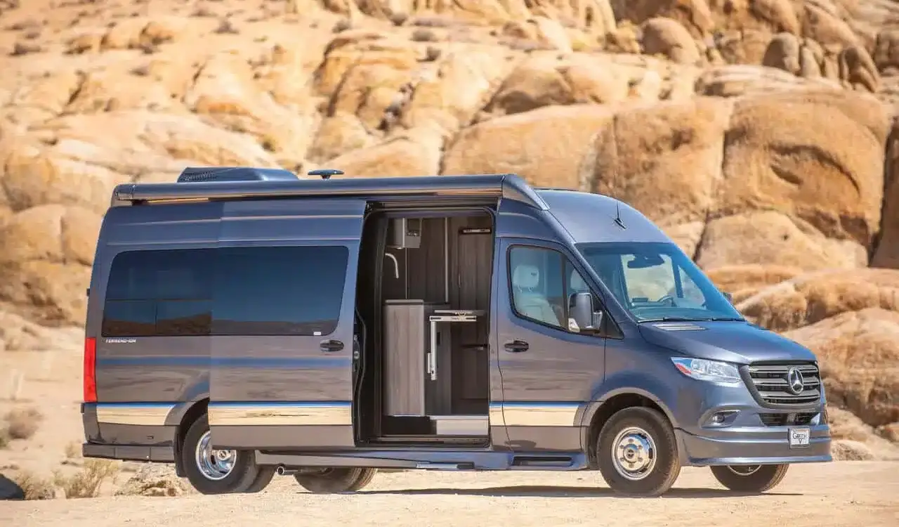 Grech Terreno-ion AWD Kastenwagen auf Mercedes-Benz Sprinter-Basis in der Wüste, seitliche Aussicht mit geöffneter Schiebetür.