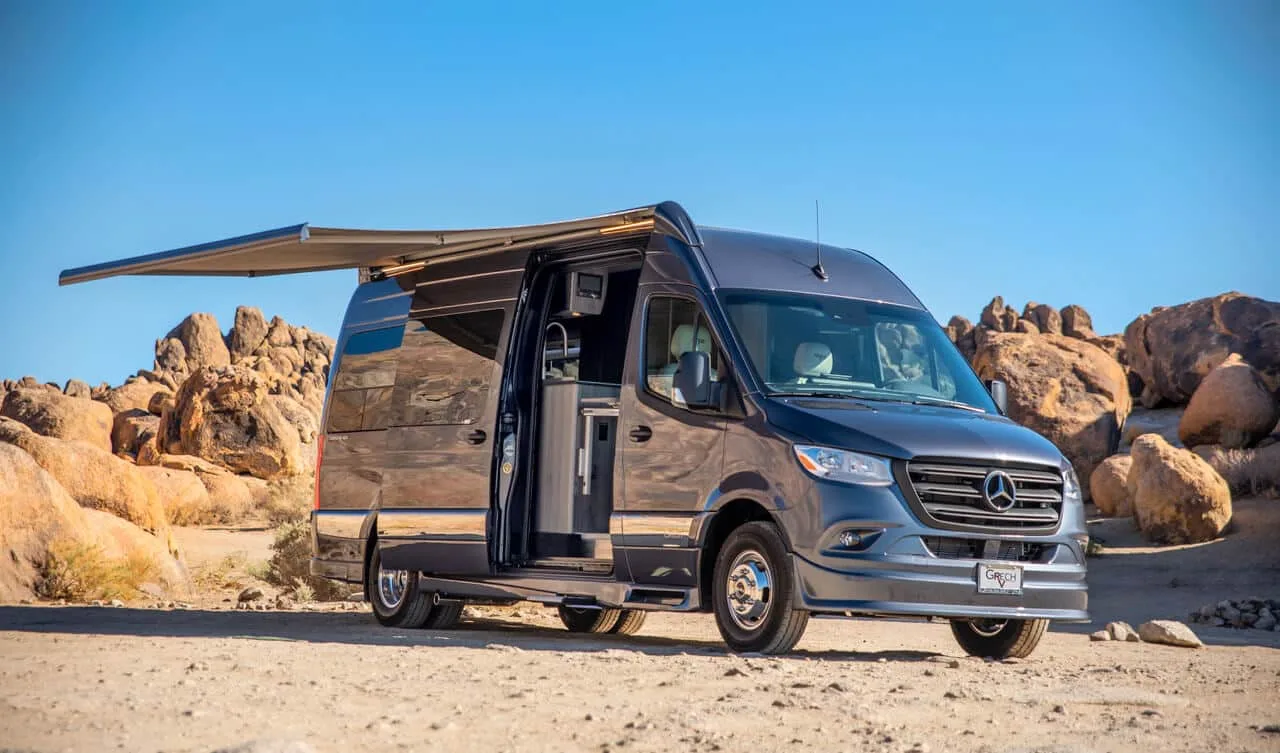 Luxuriöser Grech Terreno-ion AWD Kastenwagen, basierend auf einem Mercedes-Benz Sprinter, mit geöffneter Seitentür und Markise in felsiger Landschaft.