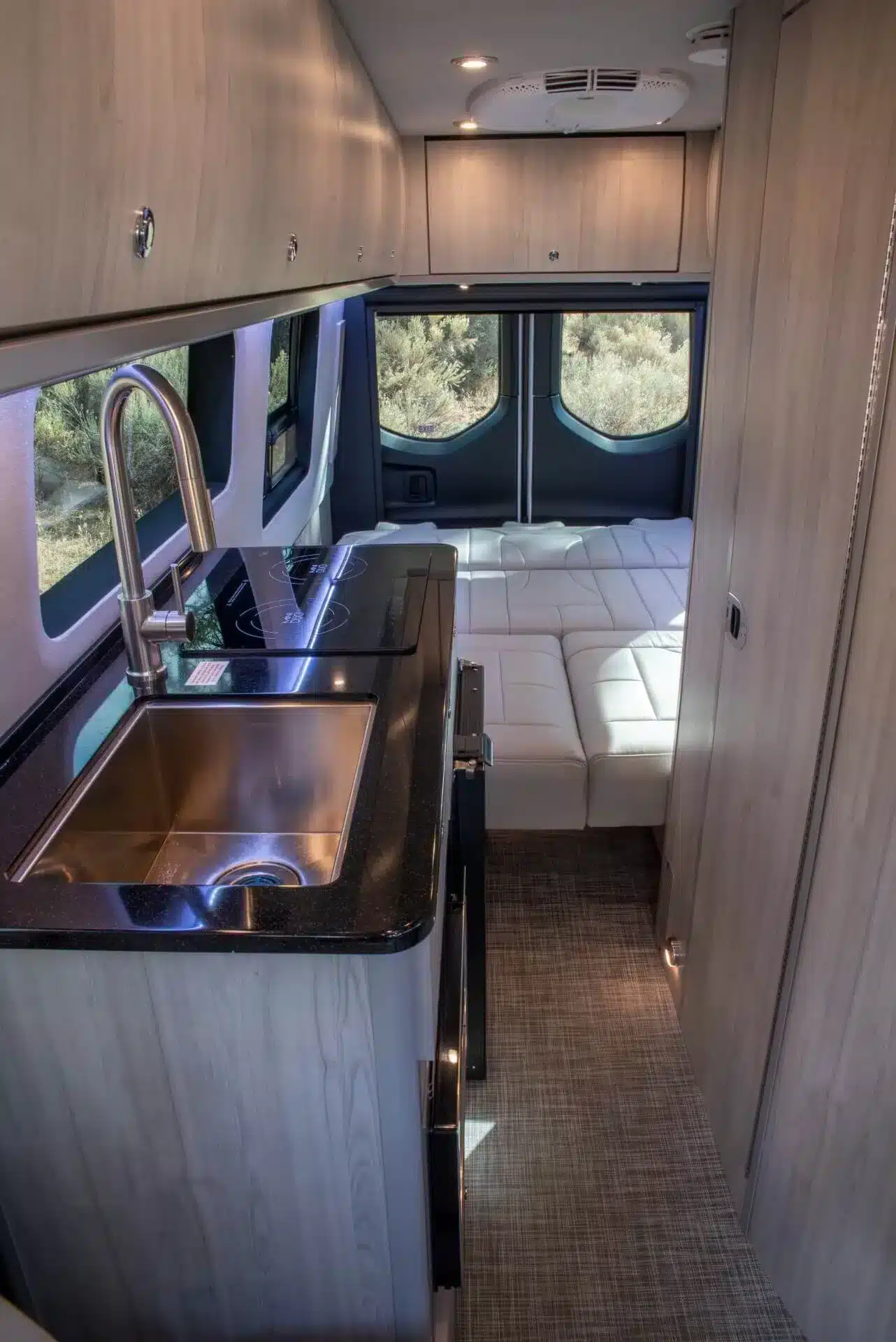 Innenraum des Grech Terreno-ion AWD mit hochwertiger Küchenzeile, Induktionskochfeld, Edelstahlspüle und Lounge-Bereich mit weißem Powersofa.