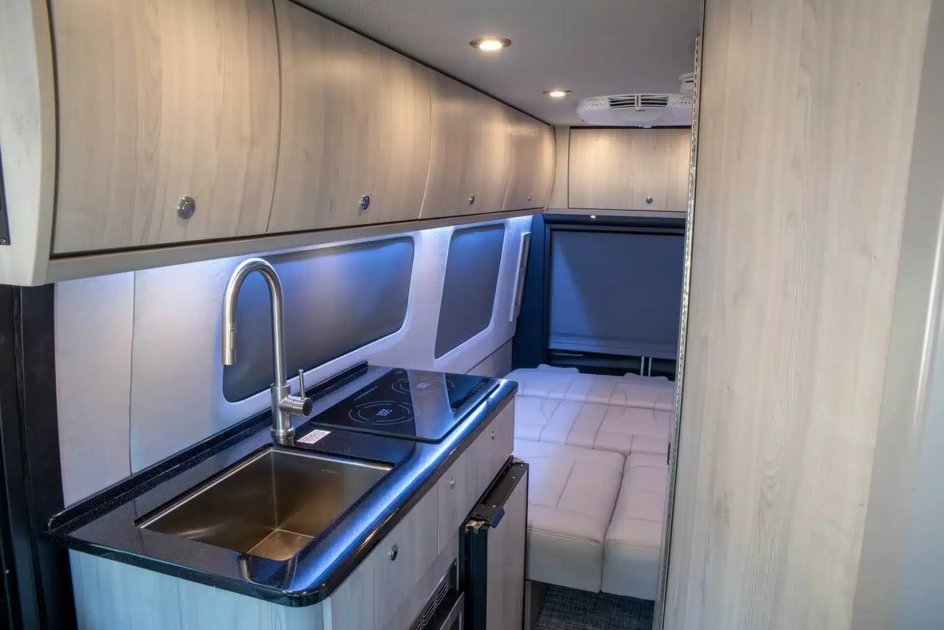 Küche und Wohnbereich im luxuriösen Grech Terreno-ion AWD Campervan mit Induktionskochfeld, Spüle und umgebautem Schlafsofa.
