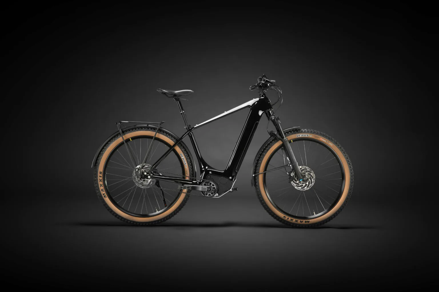 Seitliche Ansicht des schwarzen Heritage Style Escapade E-Tourenrads mit braunen Reifen und Gepäckträger vor dunklem Hintergrund.