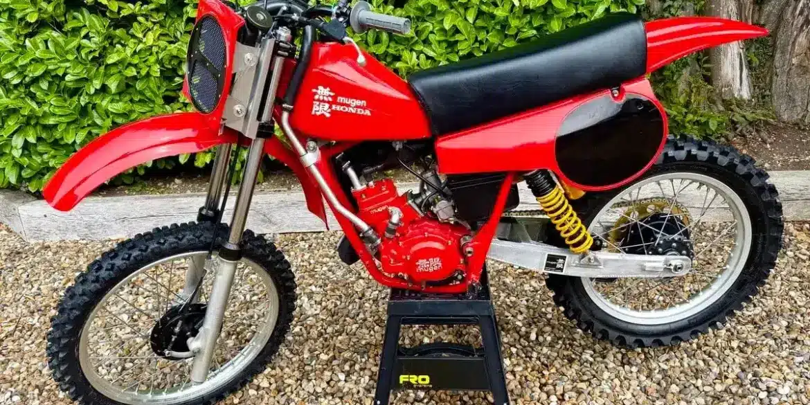 Rote Honda CR 125 von 1980 mit Mugen-Banzai-Konversion, Aluminiumtank, Öhlins-Federbeinen und am Gabeljoch montiertem Kühler, seitlich fotografiert.