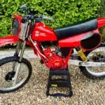 Rote Honda CR 125 von 1980 mit Mugen-Banzai-Konversion, Aluminiumtank, Öhlins-Federbeinen und am Gabeljoch montiertem Kühler, seitlich fotografiert.