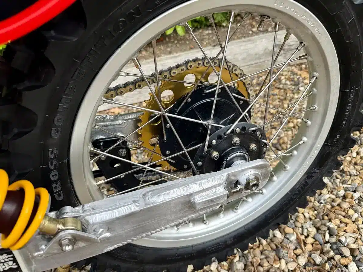 Detailaufnahme des Hinterrads einer 1980er Honda CR 125 mit Mugen-Banzai-Umbau, Aluminium-Schwinge, goldfarbenem Kettenrad und Öhlins-Federbein.