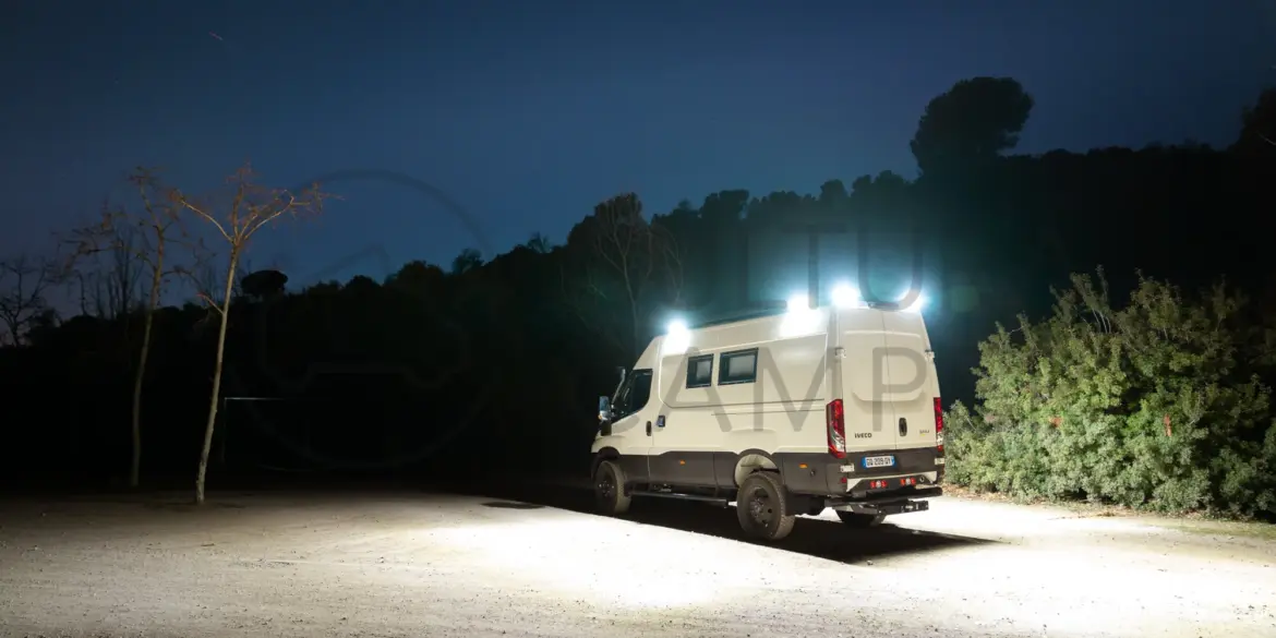 Iveco Daily 4x4 L3H2 Camper mit eingeschalteter Außenbeleuchtung bei Nacht auf offenem Gelände