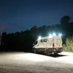 Iveco Daily 4x4 L3H2 Camper mit eingeschalteter Außenbeleuchtung bei Nacht auf offenem Gelände