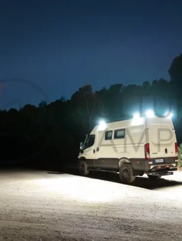 Iveco Daily 4x4 L3H2 Camper mit eingeschalteter Außenbeleuchtung bei Nacht auf offenem Gelände