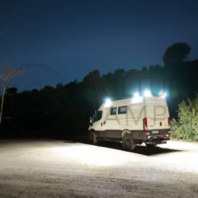 Iveco Daily 4x4 L3H2 Camper mit eingeschalteter Außenbeleuchtung bei Nacht auf offenem Gelände