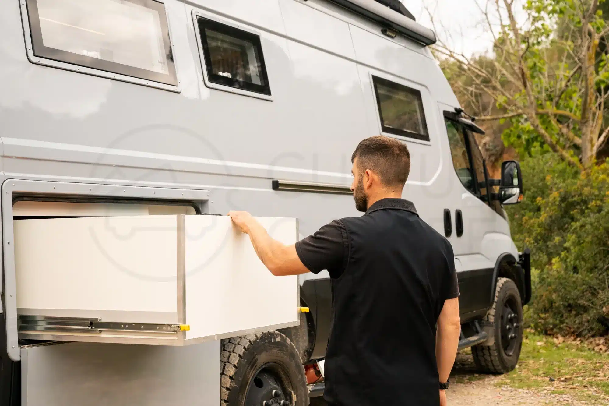 Mann bedient einen großen seitlichen Auszugstauraum an einem Iveco Daily 4x4 Expeditionsmobil.
