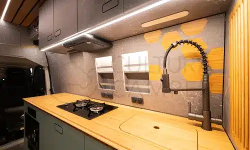 Küche mit Holzarbeitsplatte, zwei Gaskochfeldern und modernem Wasserhahn im Innenraum eines Expeditionsmobils