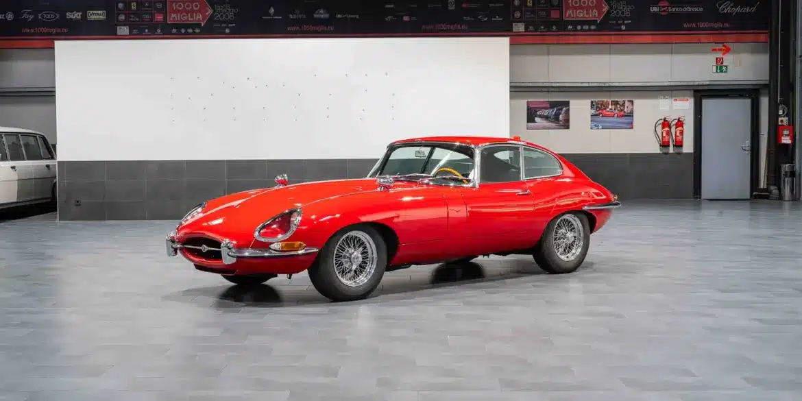 Ein rotes Jaguar E-Type Coupé Serie 1 steht in einer modernen Halle auf grauen Fliesen.