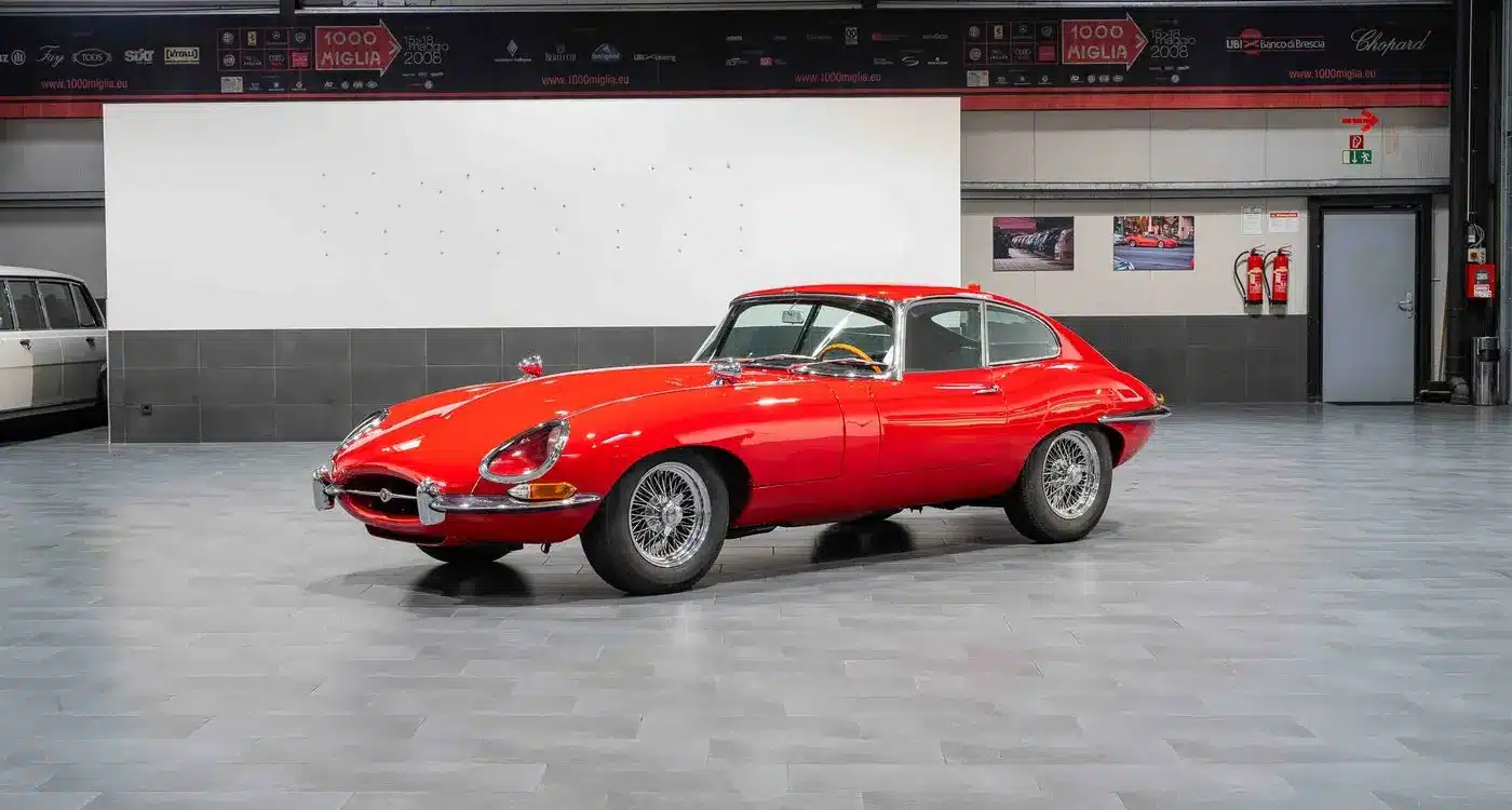 Ein rotes Jaguar E-Type Coupé Serie 1 steht in einer modernen Halle auf grauen Fliesen.
