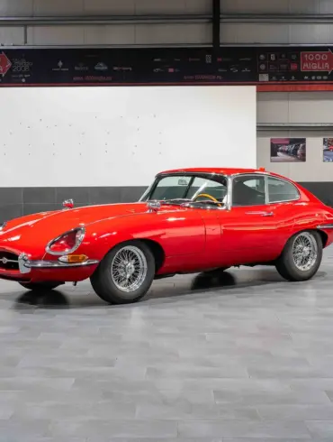 Ein rotes Jaguar E-Type Coupé Serie 1 steht in einer modernen Halle auf grauen Fliesen.