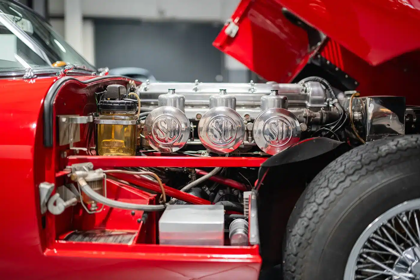 Motorraum eines Jaguar E-Type Serie 1 4.2 Roadster mit sichtbar offenem roten Kotflügel und drei SU-Vergasern